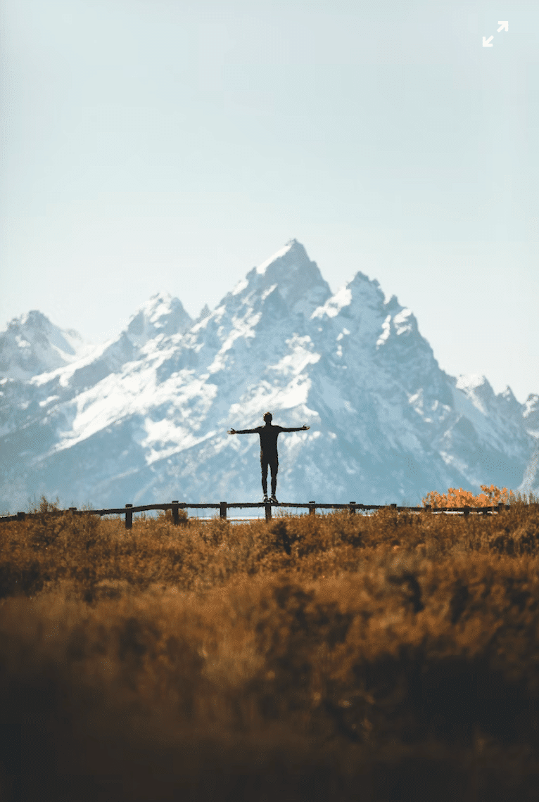 Man standing in front of a mountain with his arms out wide.